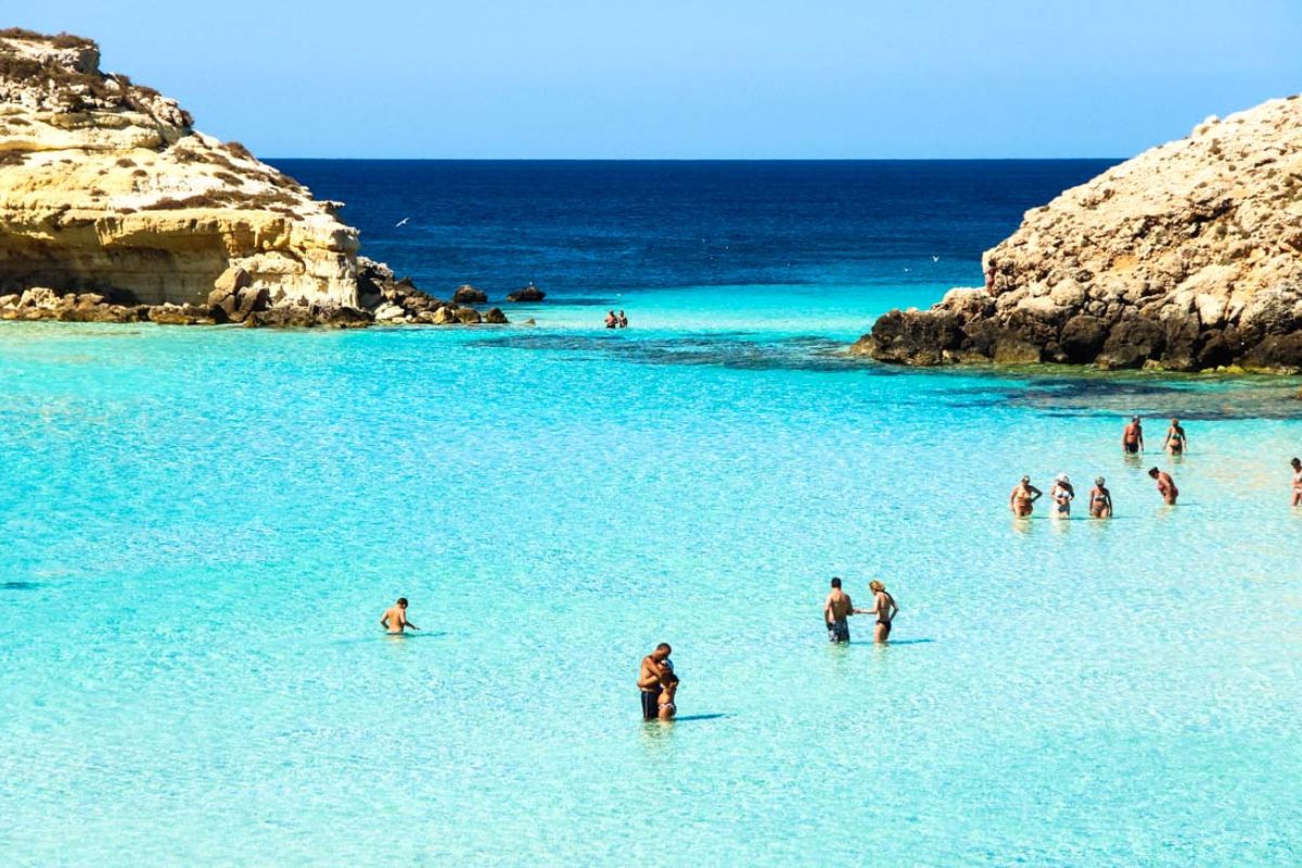 Scorcio del porto di Lampedusa al tramonto con traghetto in arrivo, colori caldi, atmosfera rilassata e vacanziera